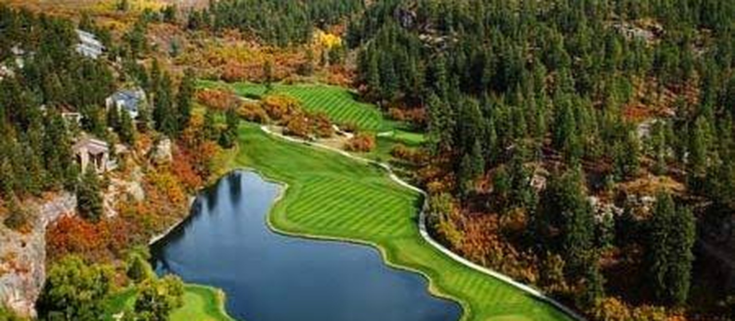 An aerial view of a mountain golf course and lake in autumn